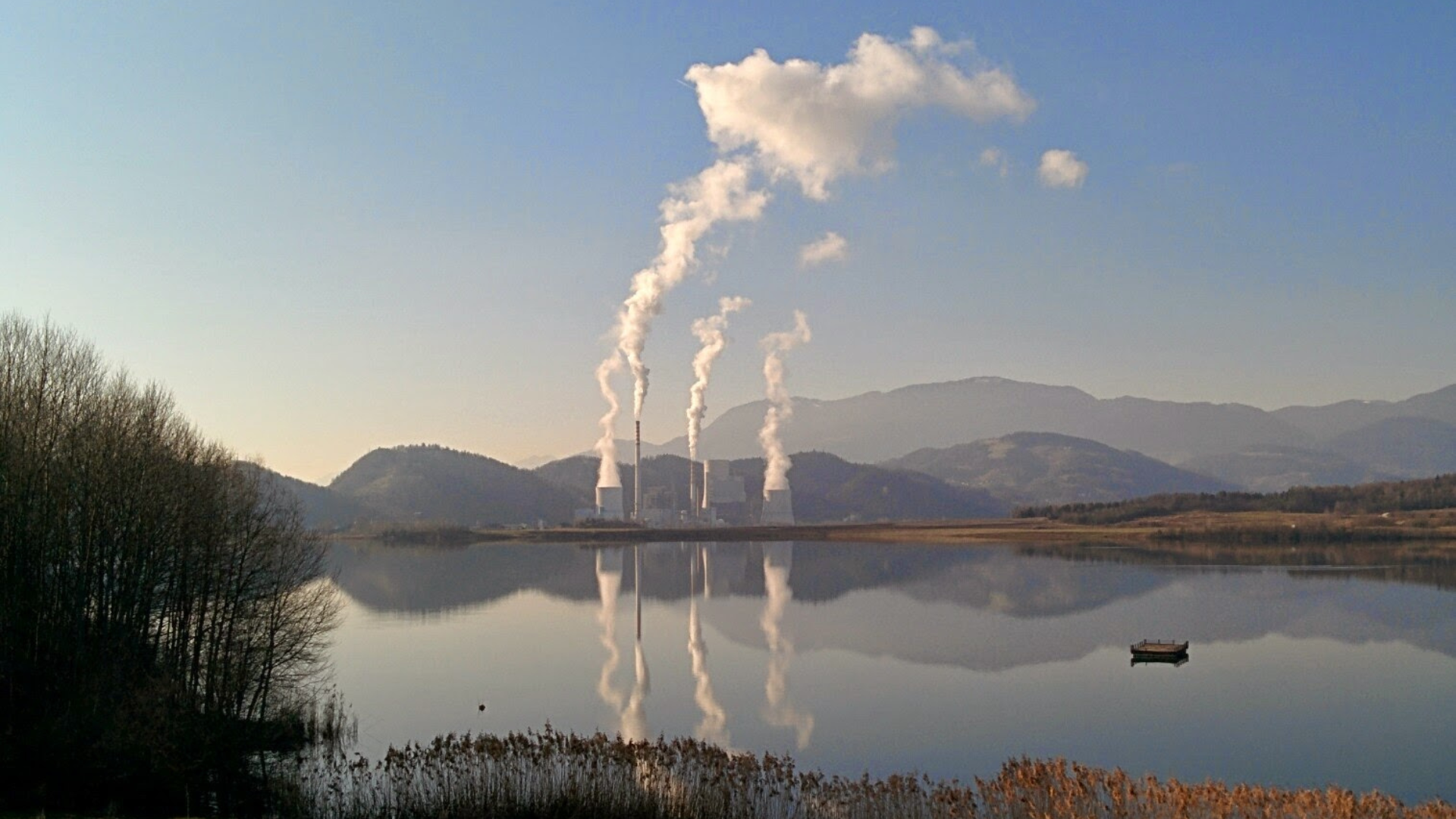 A coal powerplant next to a lake on a clear winter day. White smoke can be seen turning into clouds.