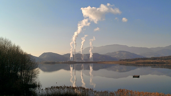 A coal powerplant next to a lake on a clear winter day. White smoke can be seen turning into clouds.